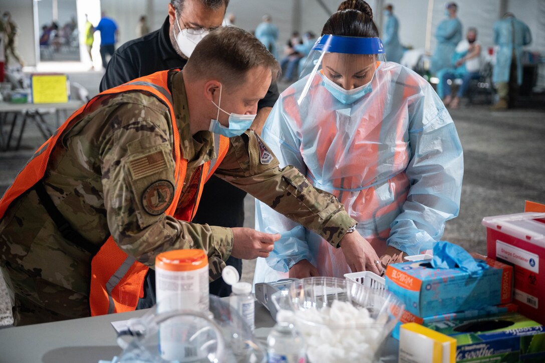 U.S. Air Force Maj. Michael Jessup (left) assists U.S. Air Force Tech. Sgt. Jerrica Wild (right), both deployed from Peterson Air Force Base, Colorado, with paper work in preparation for vaccine distribution at the Tampa Community Vaccination Center in Tampa, Florida, March 3, 2021. Jessup and Wild are two of nearly 140 Airmen on site at the state-led, federally-supported operation. U.S. Northern Command, through U.S. Army North, remains committed to providing continued, flexible Department of Defense support to the Federal Emergency Management Agency as part of the whole-of-government response to COVID-19. (U.S. Air Force photo by Master Sgt. Holly Roberts-Davis/Luke AFB Public Affairs)
