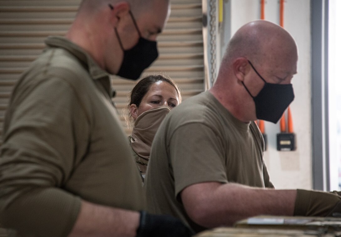 An airman inspects two munitions airmen re-labeling boxes