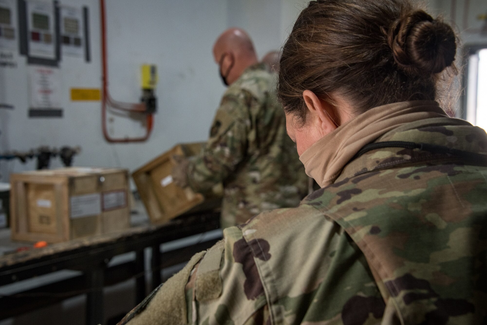 an airman in the background lifts a small wooden box while an airman in the foreground looks on