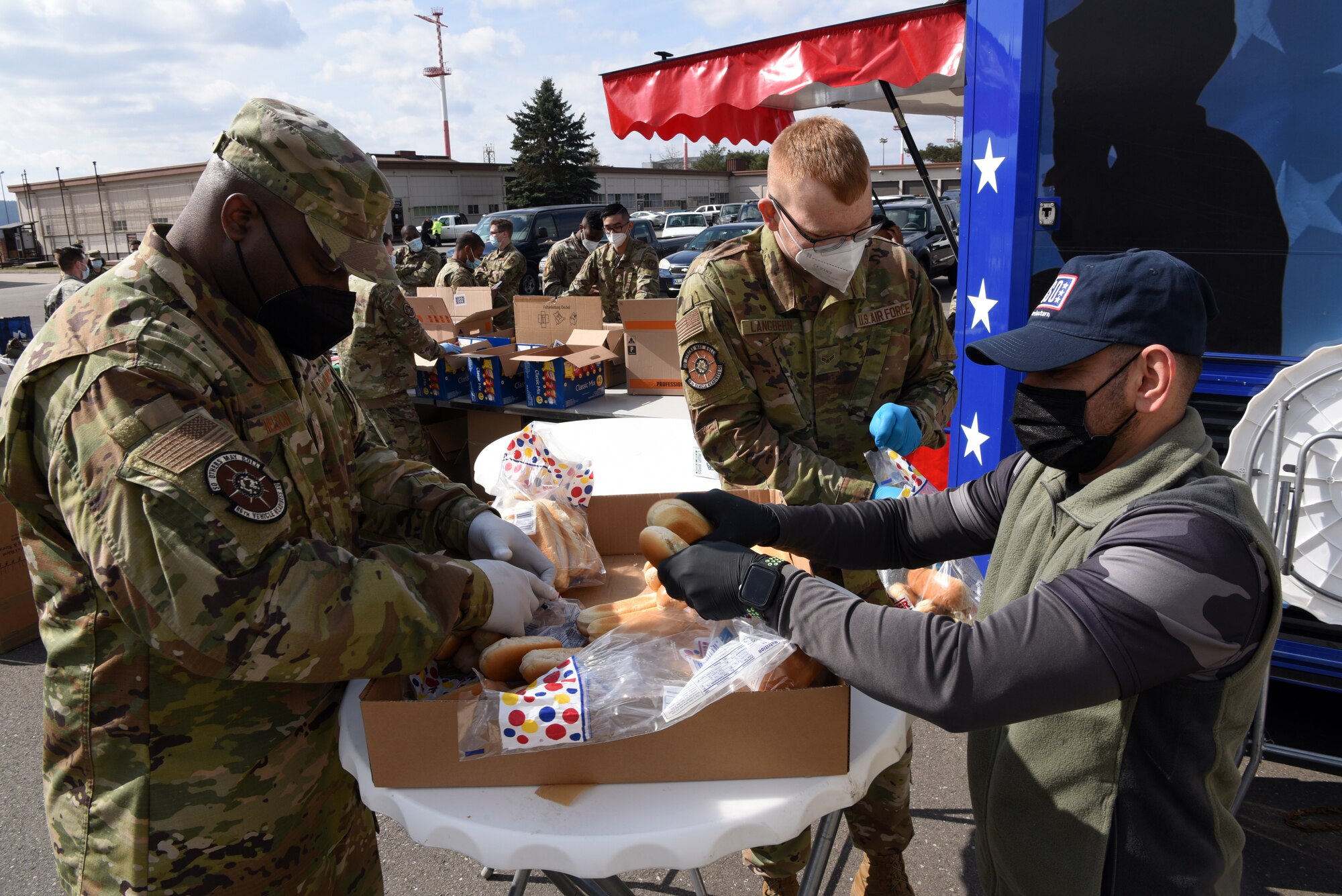 U.S. Air Force Airmen assigned to the 86th Vehicle Readiness Squadron prep hot dog buns with a USO volunteer.