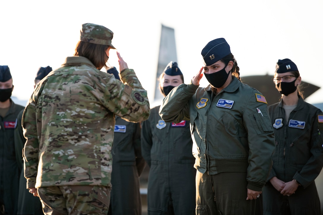 Two airmen salute each other as other service members stand in the background.