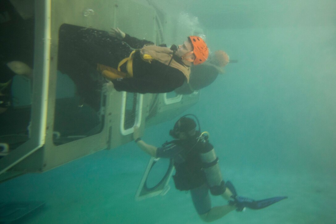 Marines exit a submerged aircraft during underwater training.