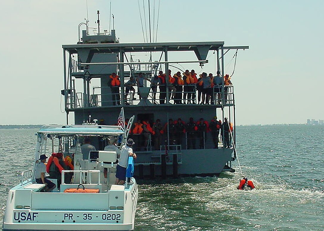 a SERE instructor demonstrates the “front drag” position while students stand on the stern observing the technique.