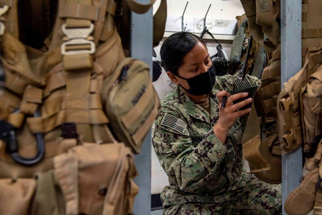 A sailor inspects military gear while kneeling on the ground.
