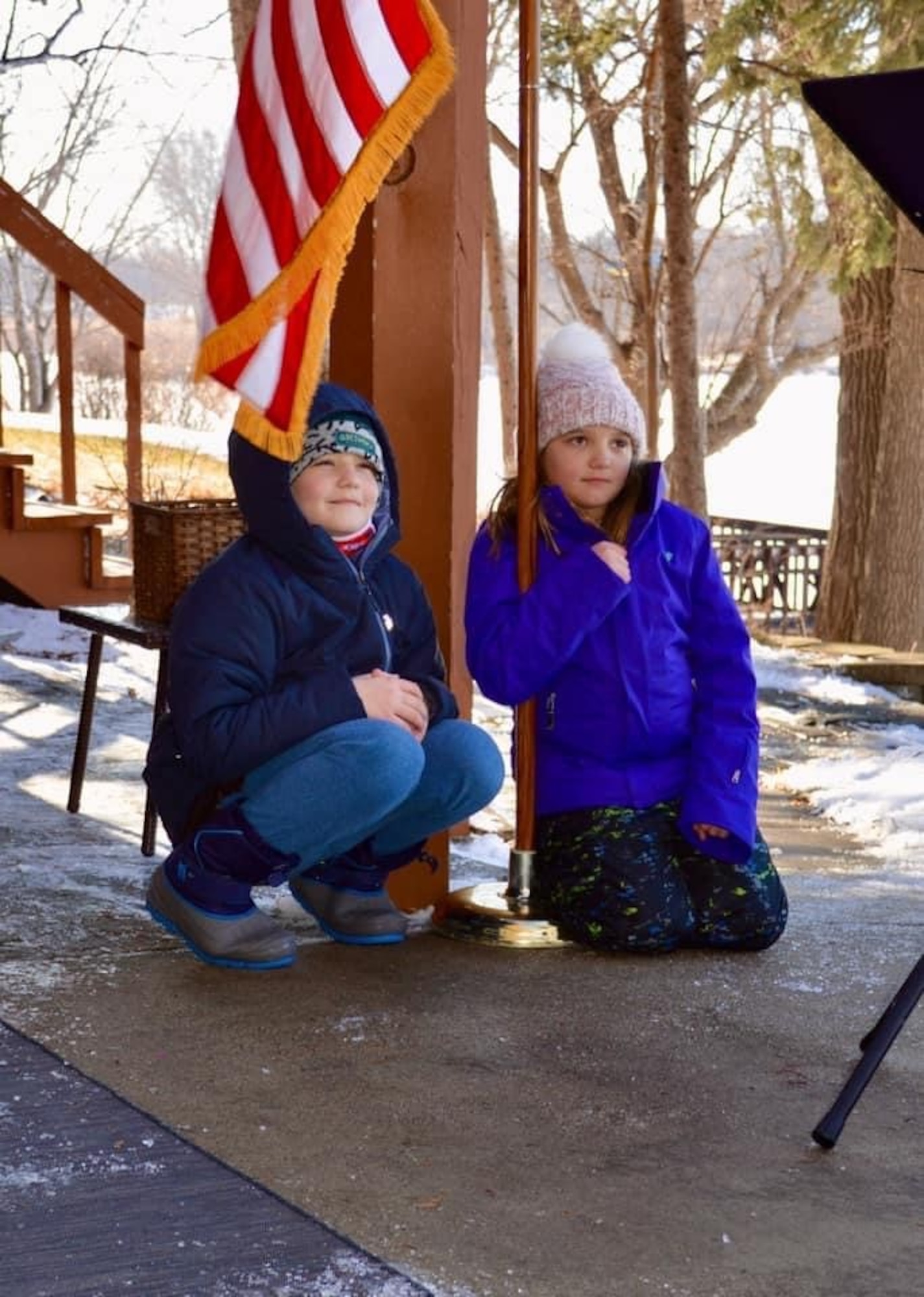 A boy and girl crouch near an American flag.