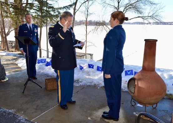 Man in uniform administers oath of office to female in uniform.