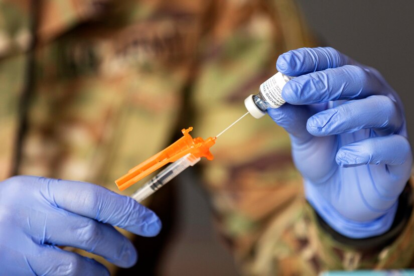 Someone wearing gloves holds a syringe which is being inserted into a vial.