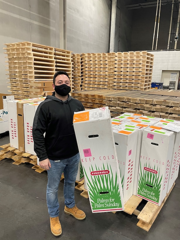 A DLA worker stands with a shipment of religious palms.