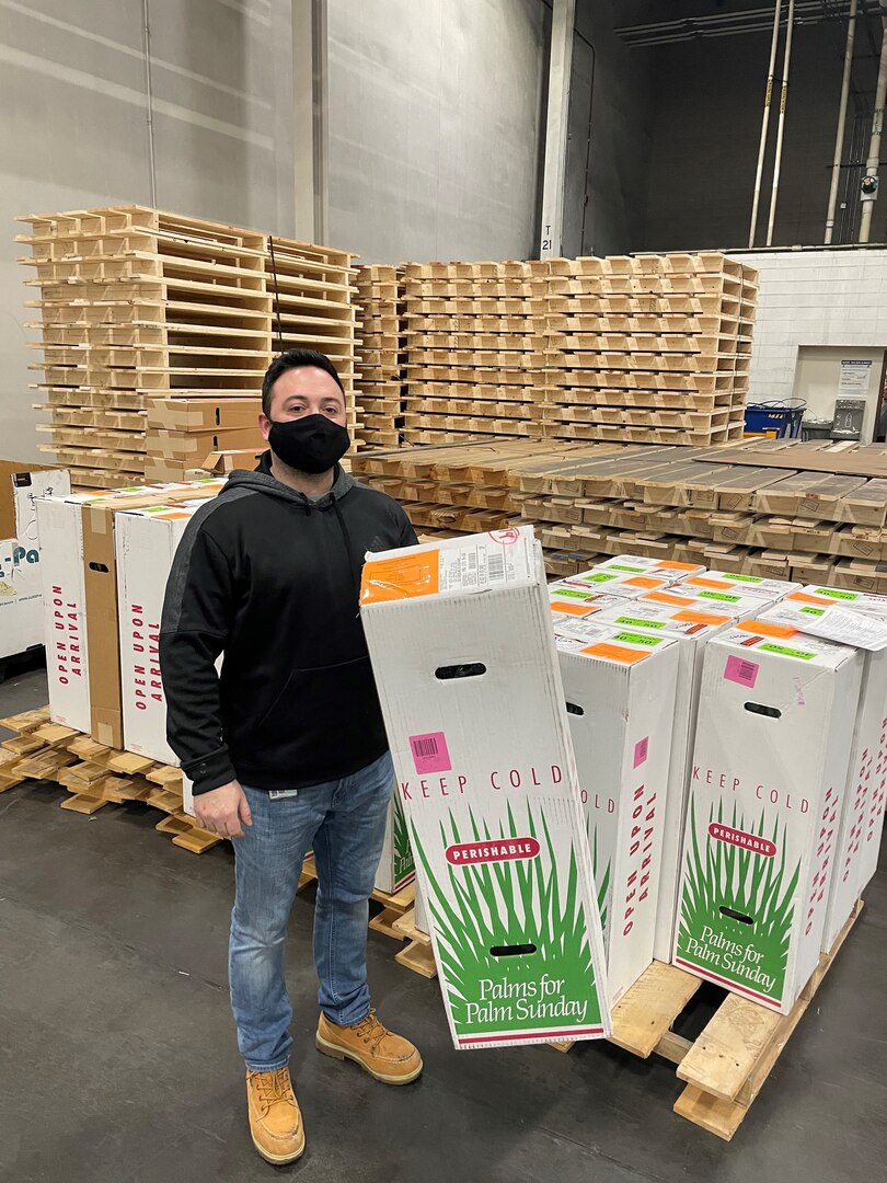 A DLA worker stands with a shipment of religious palms.