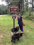 Kathy stands near a sign with two dogs