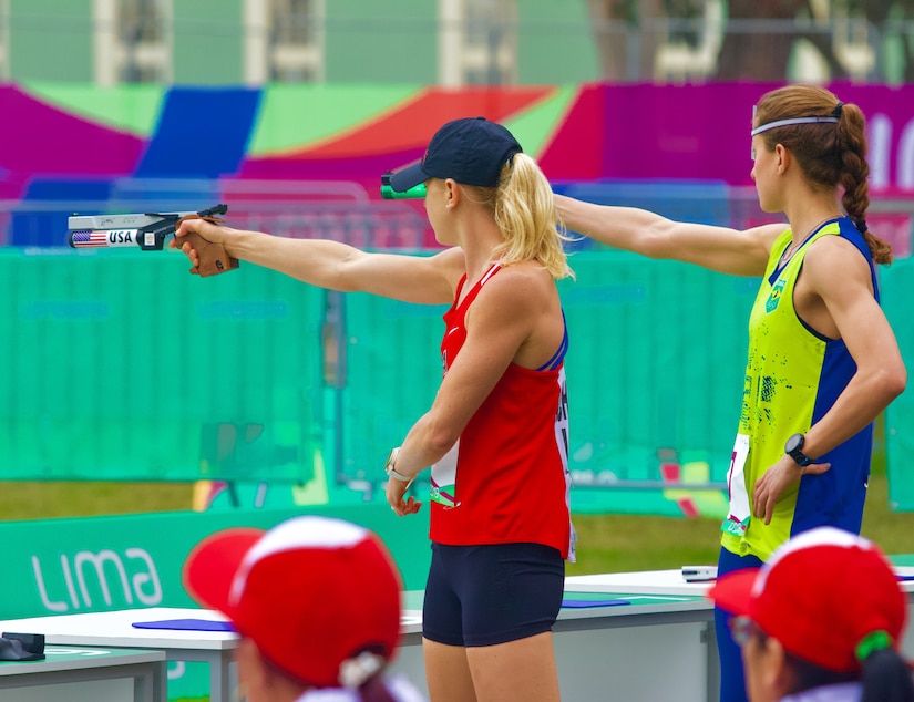 Two women shoot handguns at a competition course.