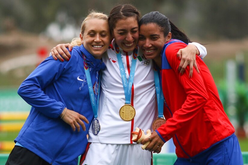 Three women wearing sports uniforms and medals around their necks hug one another.