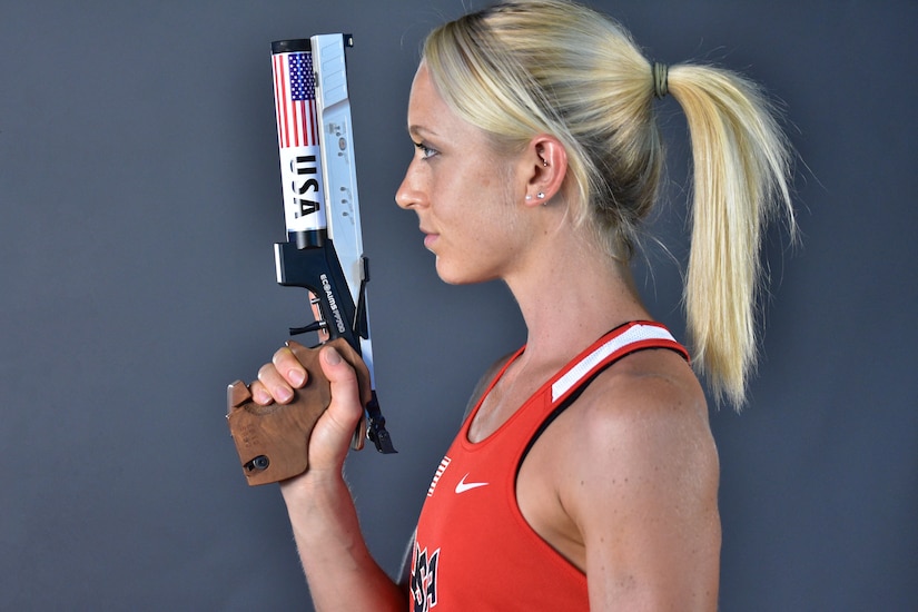 A woman wearing a competition jersey holds a pistol used in competition.
