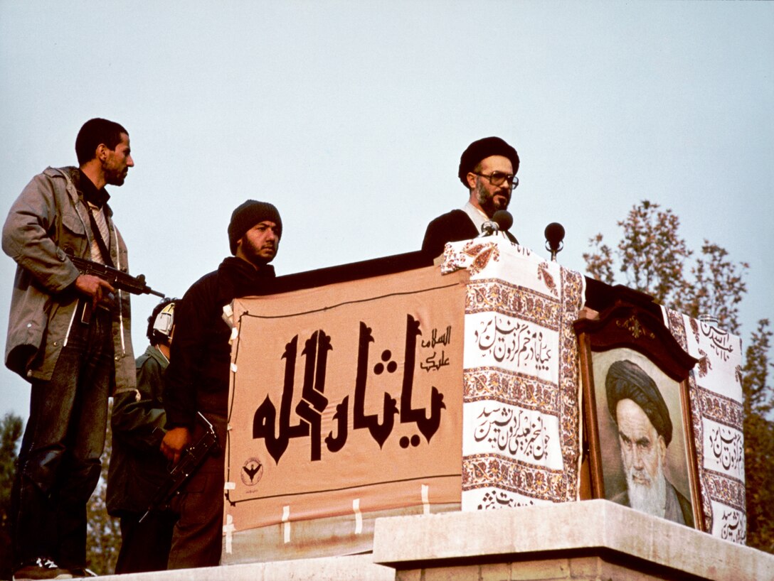 Muslim cleric, possibly Mohammad Mousavi Khoeiniha, speaking behind cloth-drapped stand displaying photograph of Ayatollah Khomeini, outside U.S. Embassy, Tehran, Iran, 1979 (Library of Congress/Sharok Hatami)