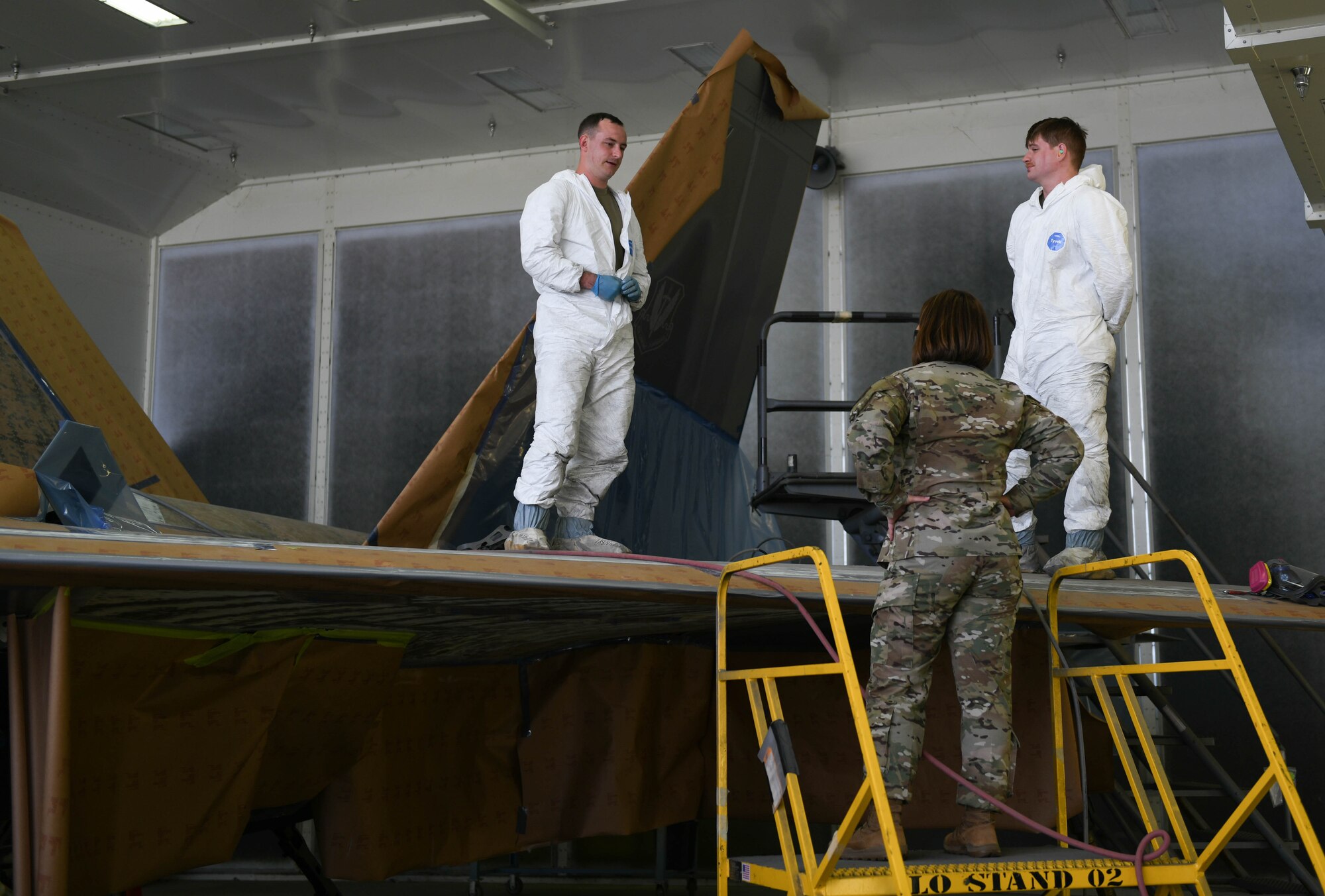 Chief Bass stands on a ladder talking to Airmen working on an F-22 Raptor.