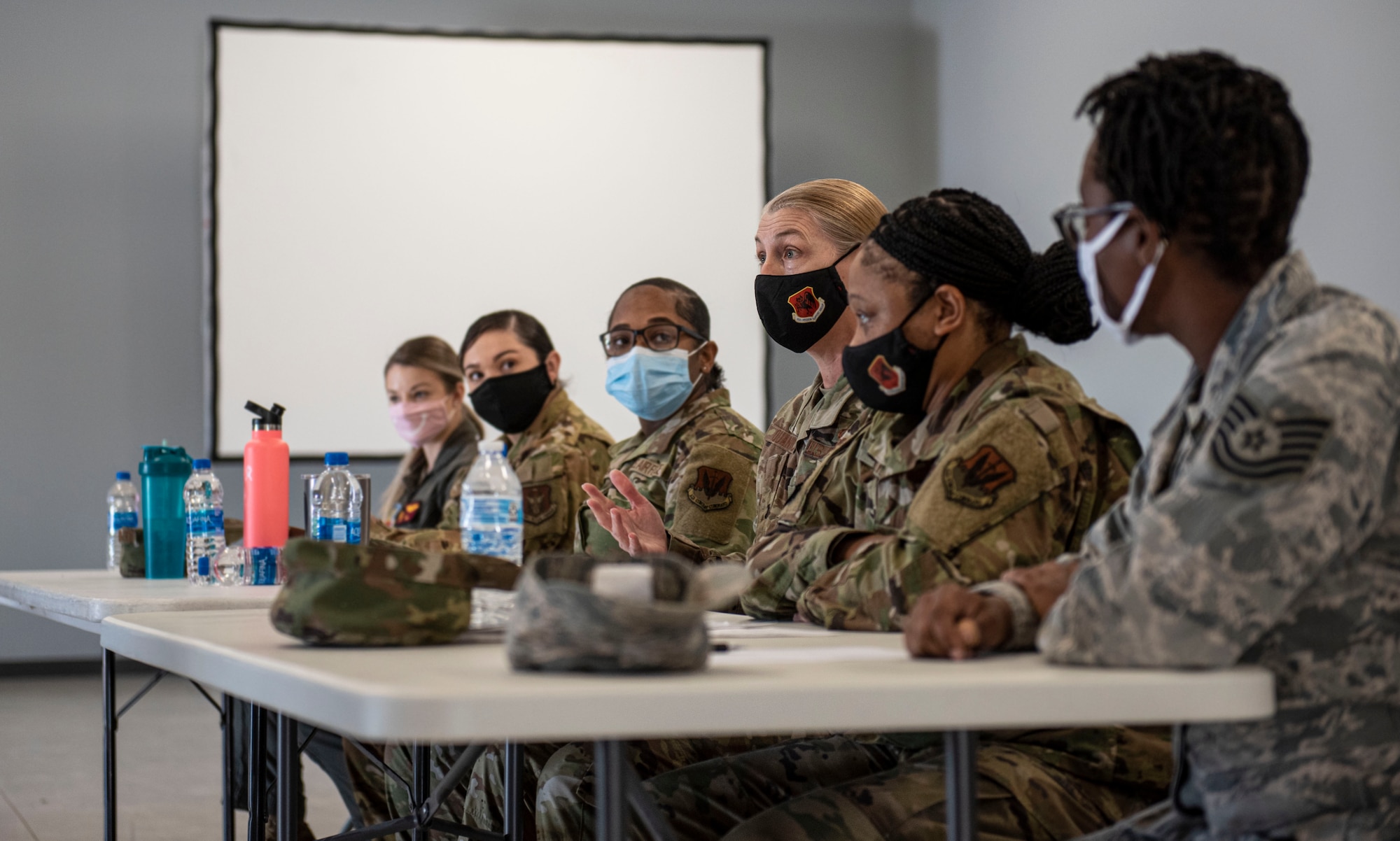 One female Airman in a line of six seated at a table is speaking.