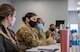 One female Airman, in a line of six seated at a table is speaking.