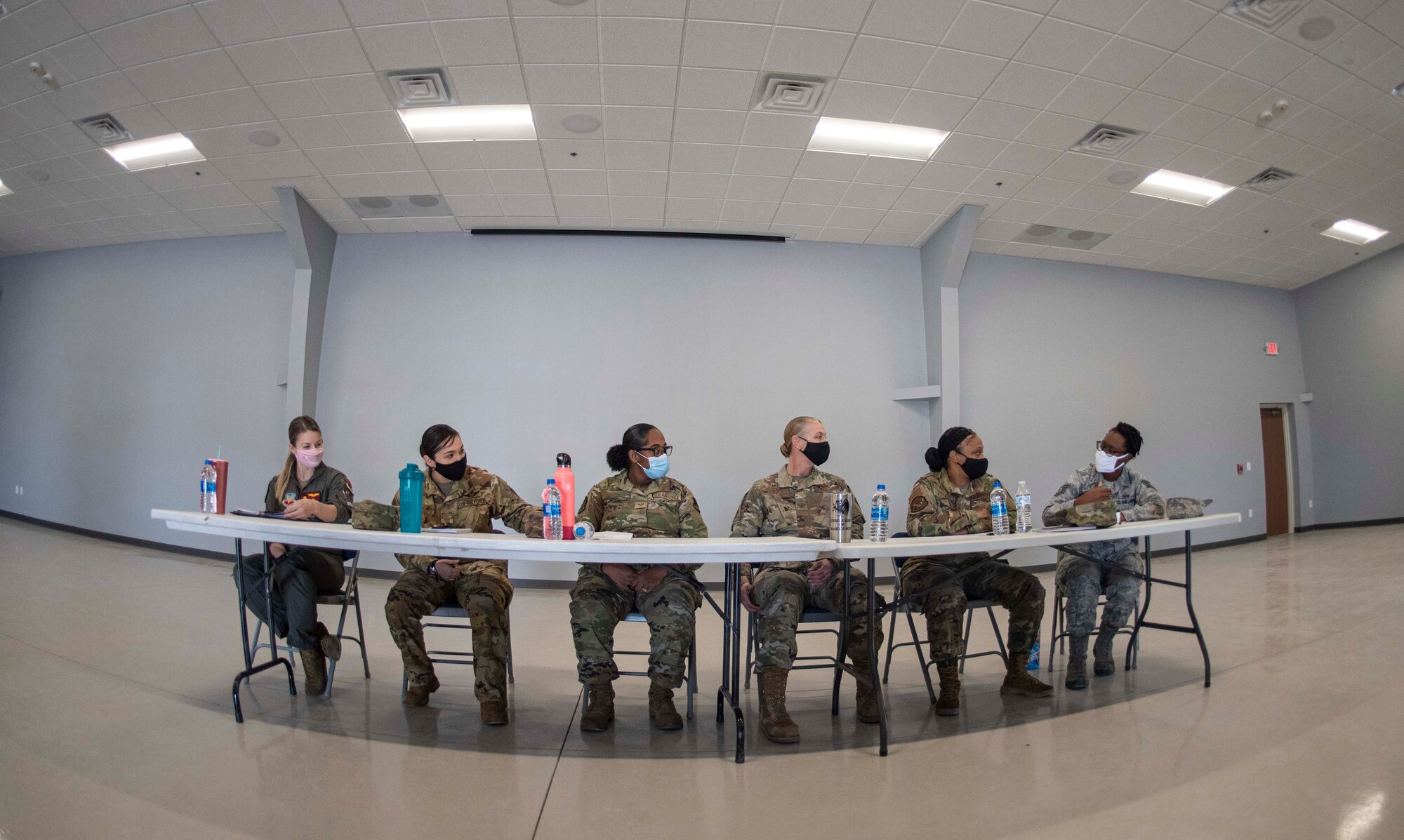 Six female Airmen are sitting at a table and talk with each other.