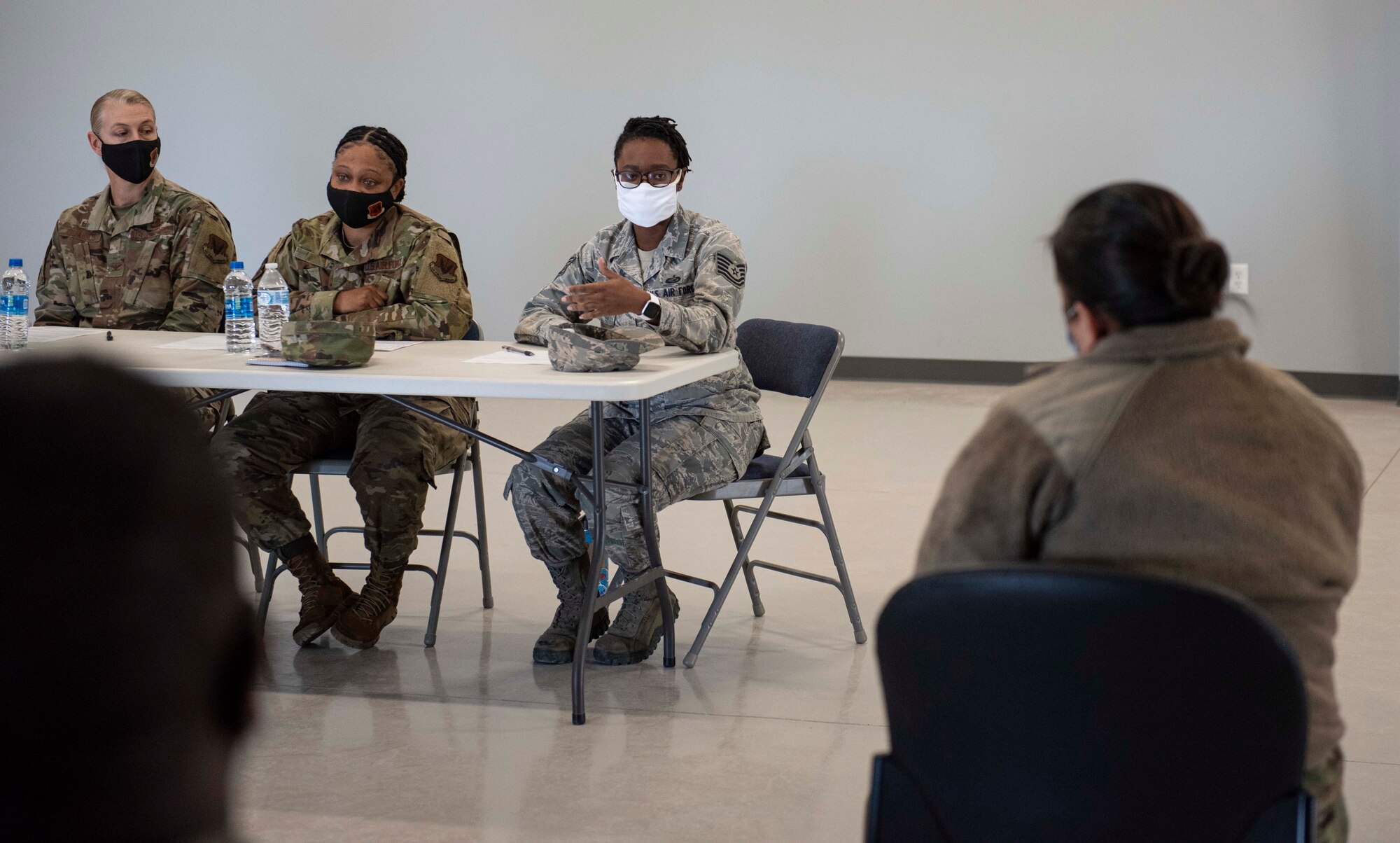 The back of a female Airmen facing three female Airmen sitting at a table. One at the table is talking.