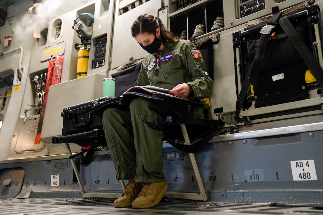 An airmen wearing a mask reads a book.