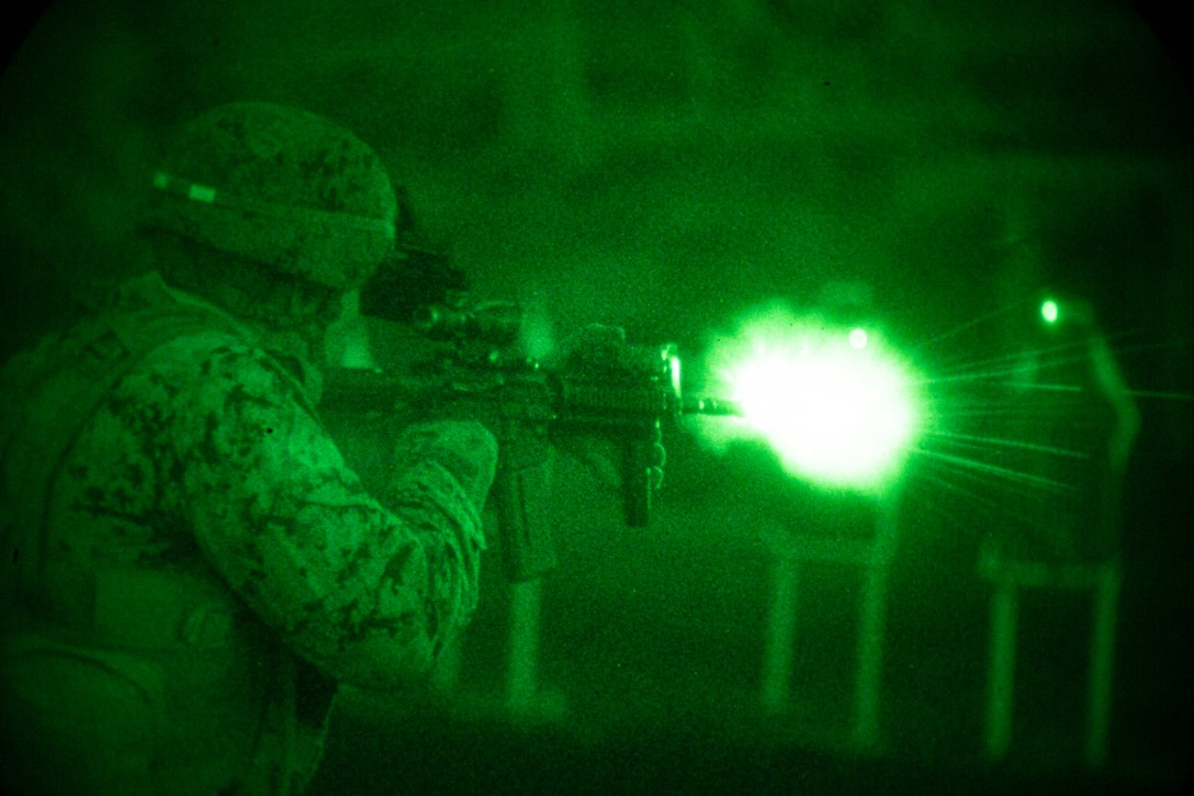 A Marine fires a weapon in the dark.