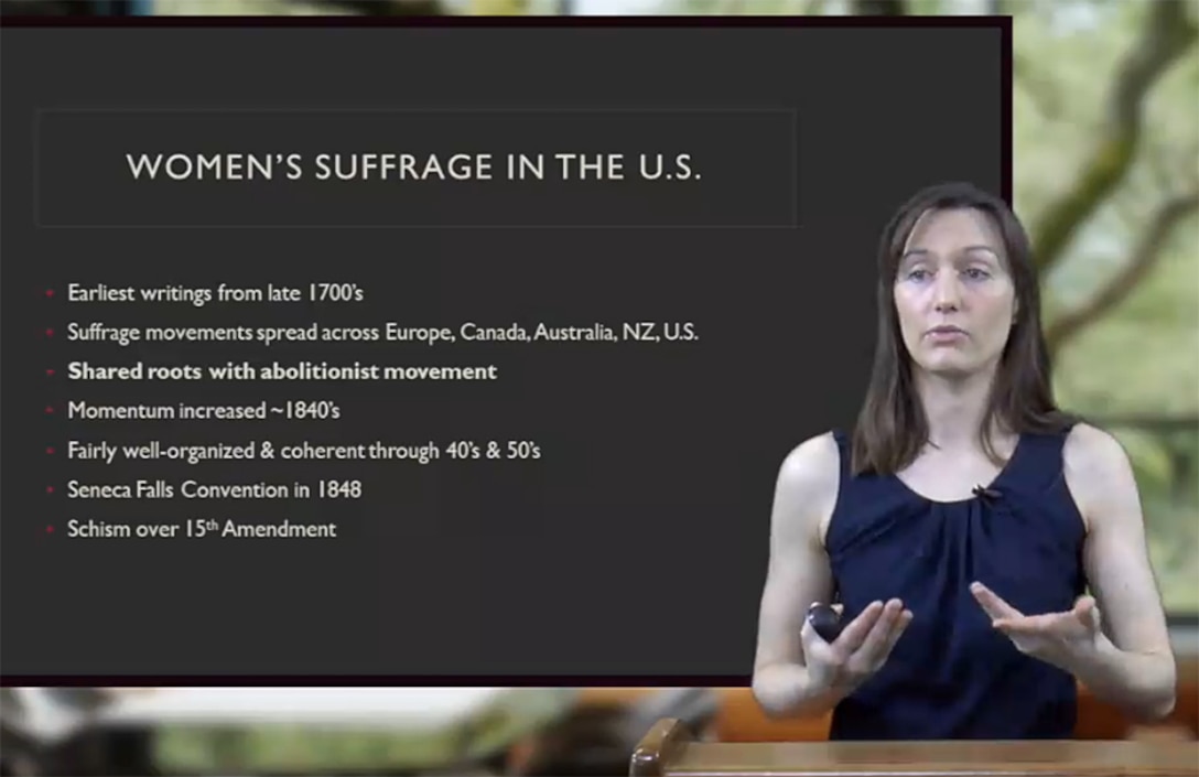 A woman speaks in front of a digital blackboard.