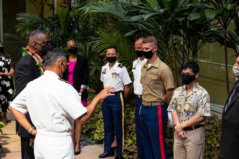 Two men, one in a uniform and one in a suit, talk to three service members and two people dressed in civilian clothing.