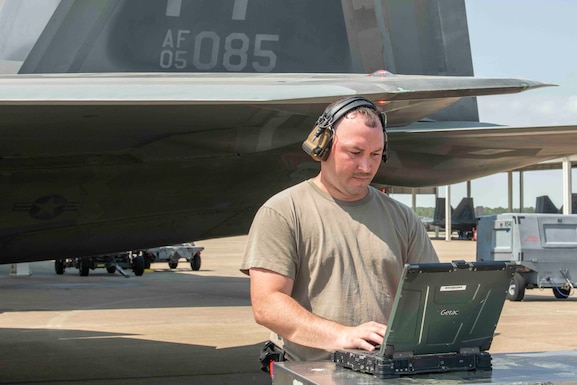 A crew chief checks his computer next to an F-22 Raptor