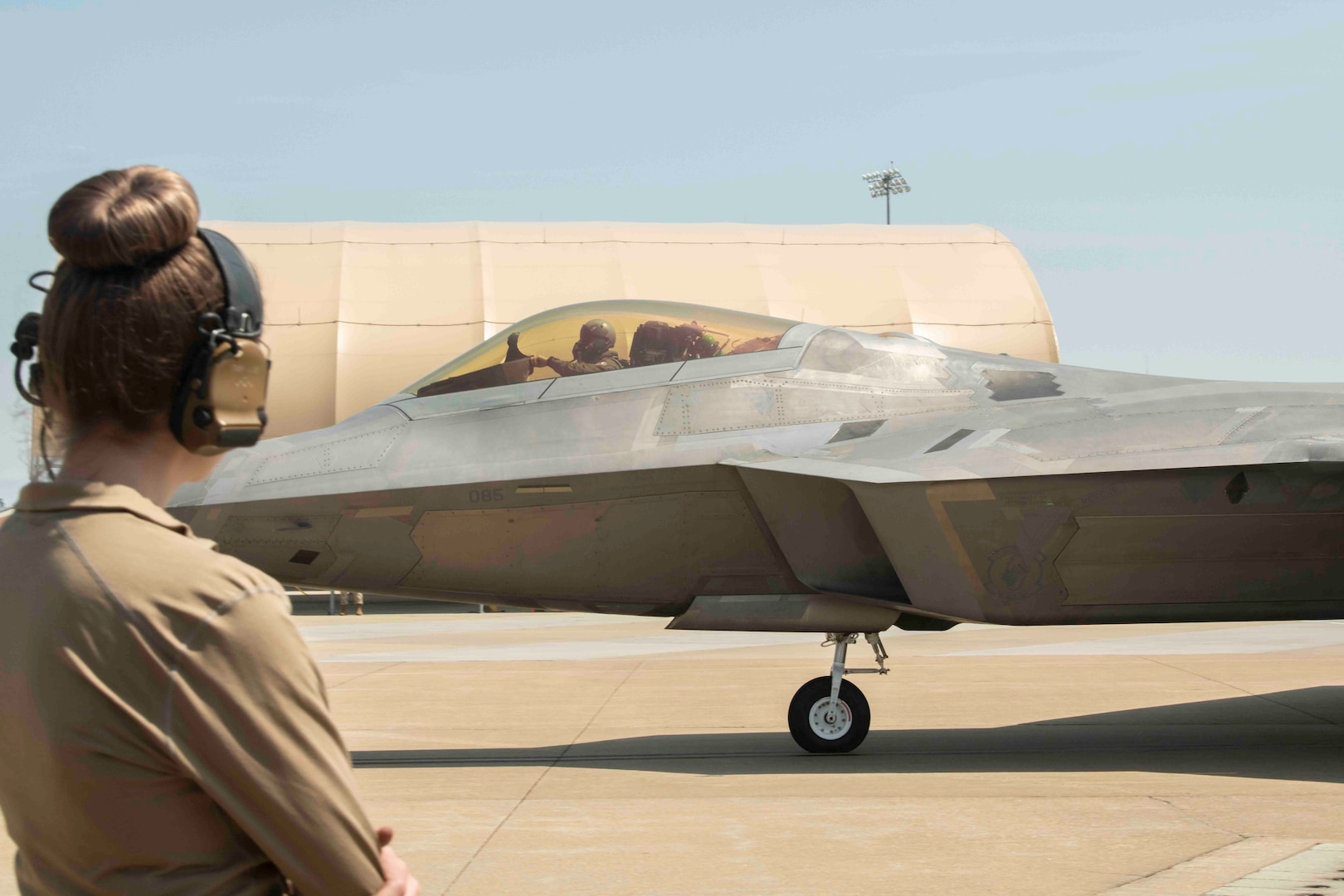 An airman looks on as F-22 tail #85 taxies towards its first flight in more than a year