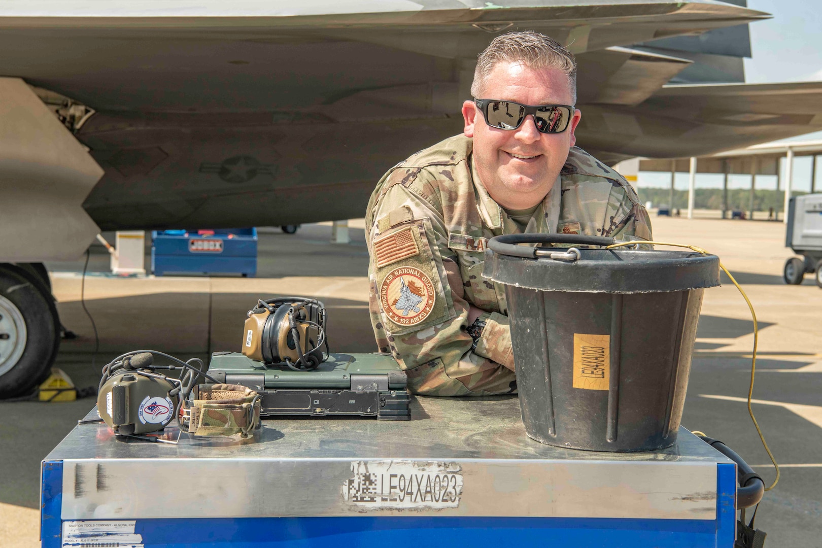 A crew chief smiles for a photo next to an F-22 Raptor