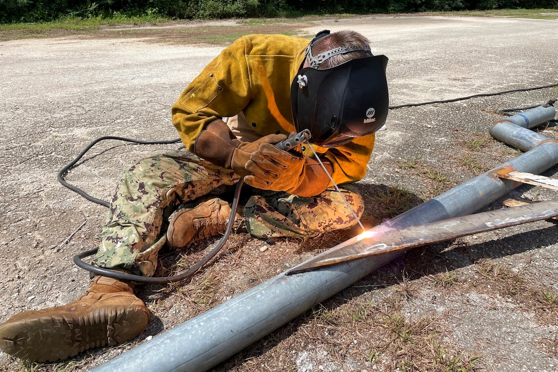 A sailors welds a metal pipe as sparks fly.