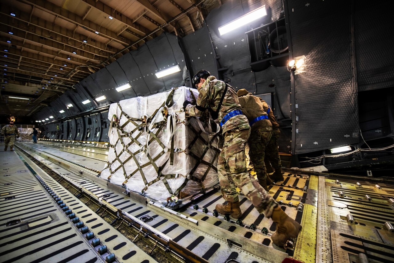 Several airmen wearing face masks and gloves push pallets of COVID-19 supplies to assist India.