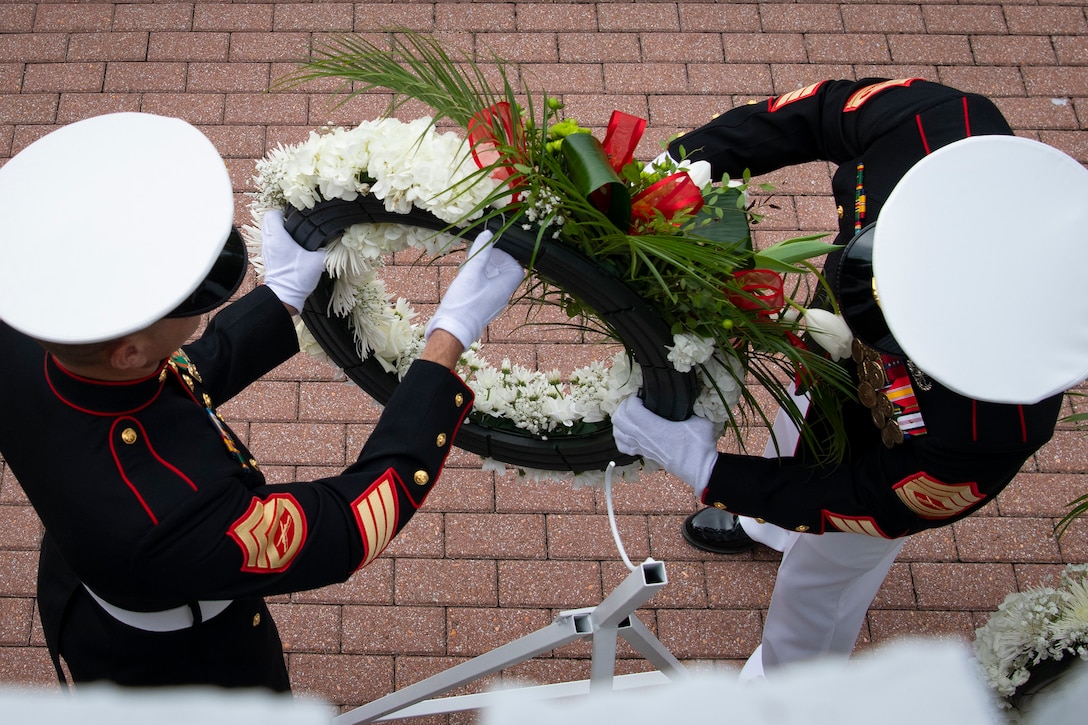Two Marines, seen from overhead, handle a wreath while standing on a brick surface.
