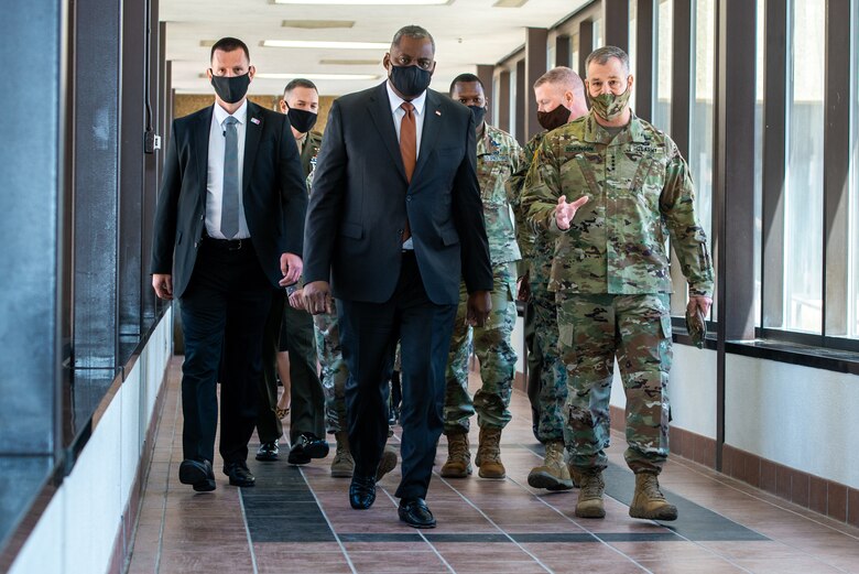 Secretary of Defense and other military personnel walking down a hallway talking to each other.
