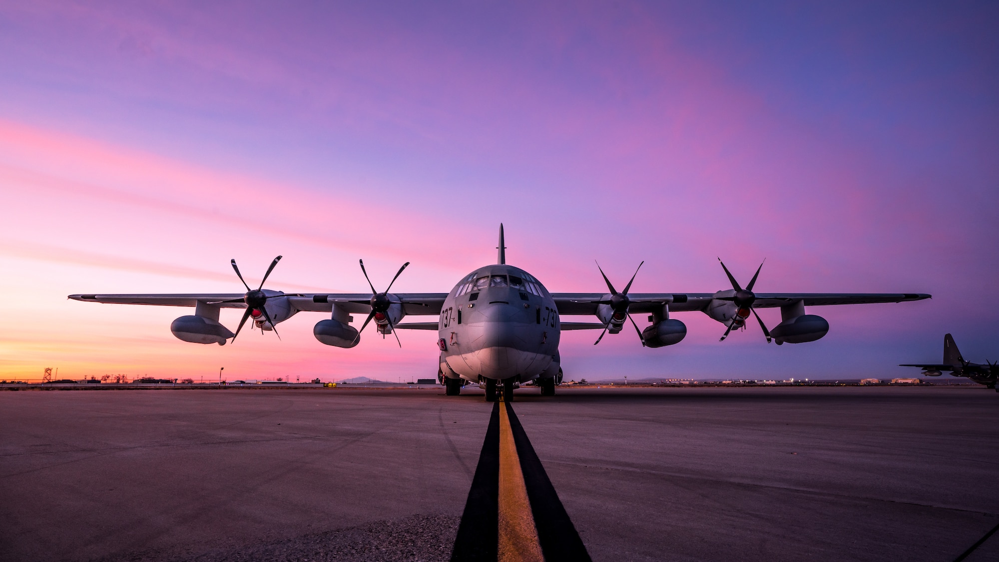 A C-130 sits parked on the flight line while the sunrise happens behind it