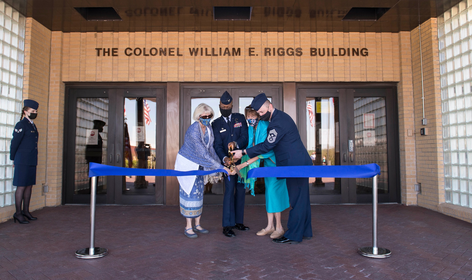 Two women and two uniformed men cut a ribbon in front of a building.