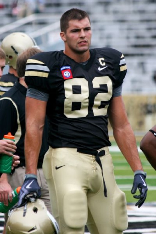 A football player stands on a football field holding his helmet.