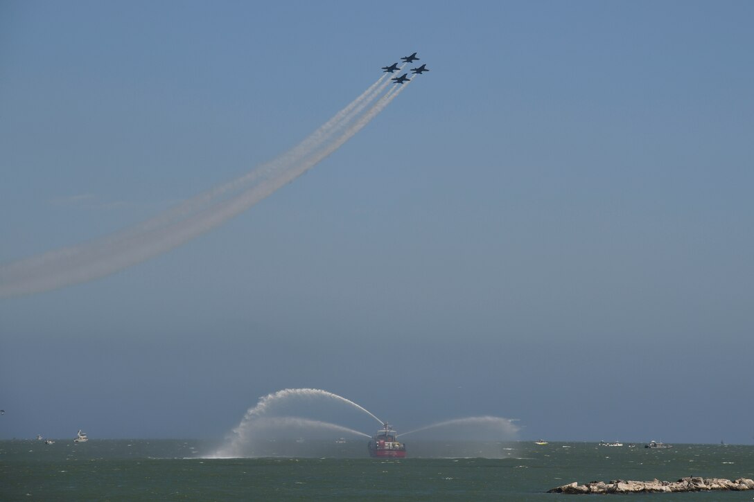 Aircraft fly over a small boat spraying water while transiting a body of water.