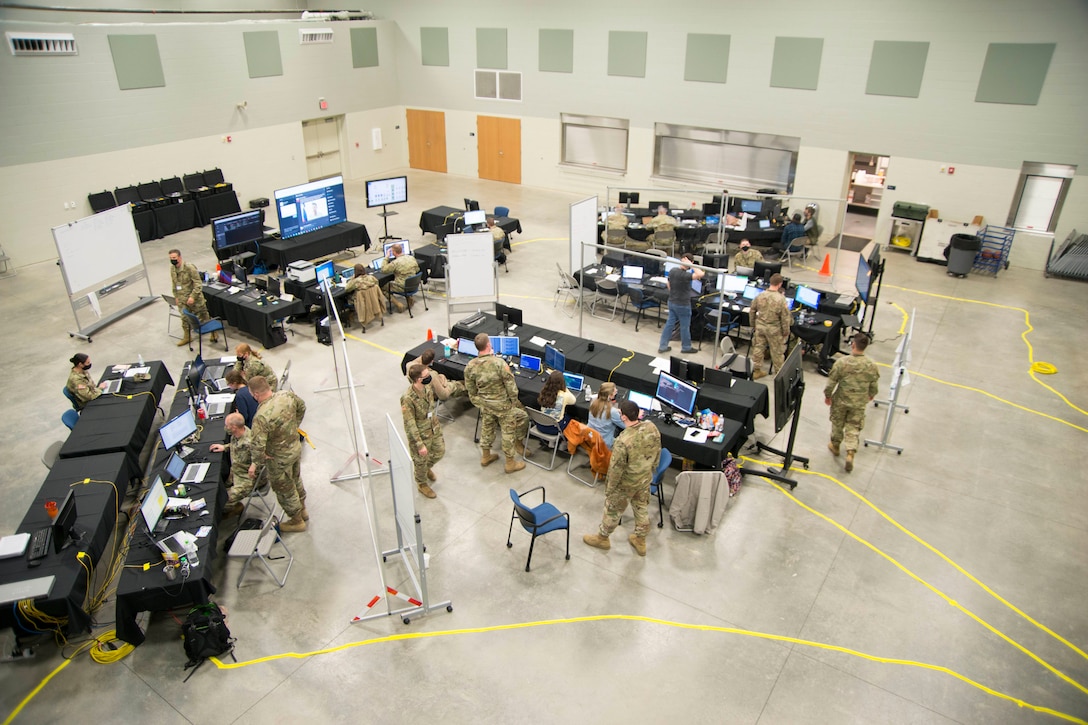 Service members work at long tables in a big room.