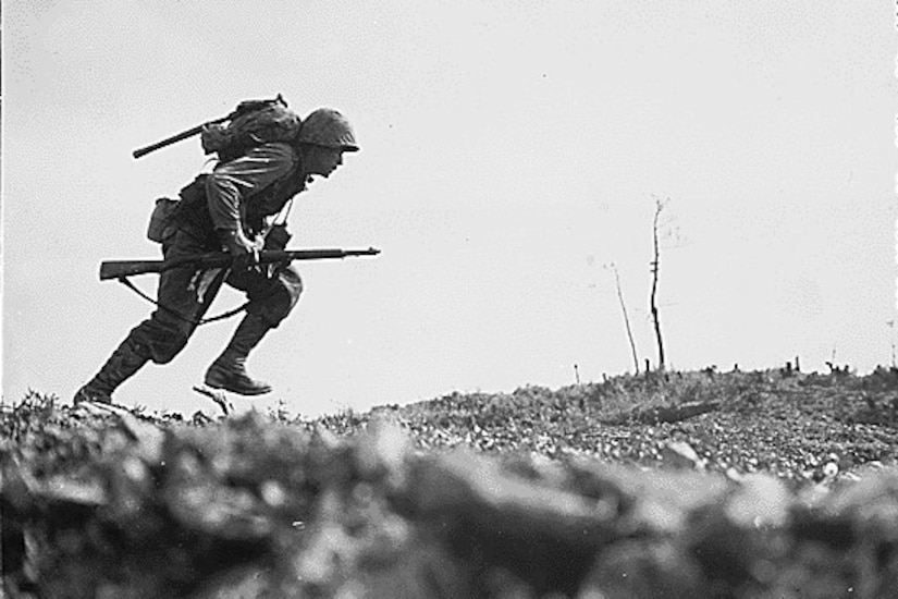 A man with a rifle sprints across a flat surface.