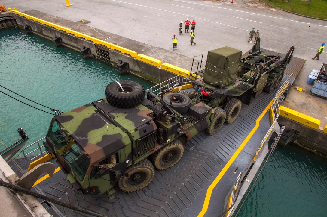 A large military vehicle is loaded onto a ship.