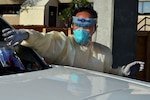 A sailor in personal protective gear handles a test kit at a drive-through COVID-19 test site.