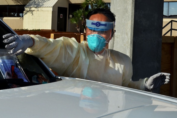 A sailor in personal protective gear handles a test kit at a drive-through COVID-19 test site.