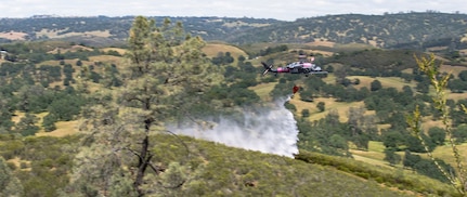 A U.S. Air Force HH-60 Pave Hawk rescue helicopter from the 129th Rescue Wing, California National Guard, deploys its water bucket on a simulated fire during annual joint aerial fire fighting training near Ione, California, April 24, 2021.