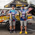 two men standing in front of a boat, holding fish.