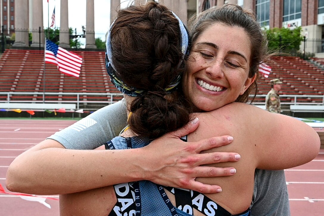 A National Guard member smiles while hugging a fellow member, both in running gear, on a track.