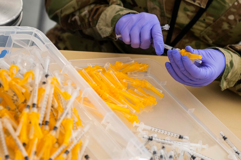 An airman wearing gloves assembles syringes that will be used in the distribution of  vaccines.