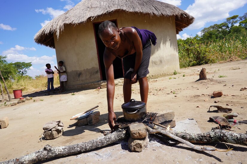 A woman tends a small pot sitting on an open fire.