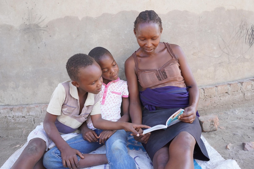 A woman and two children sit on a blanket and look at a book.