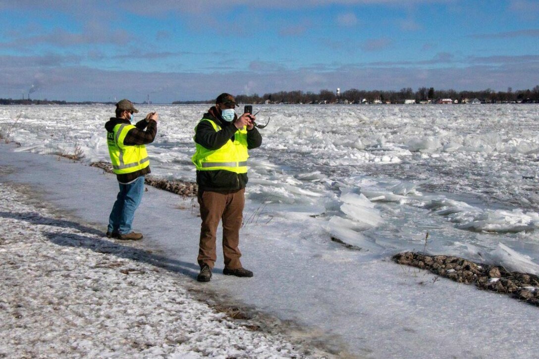 Two men take photos of ice on a river.